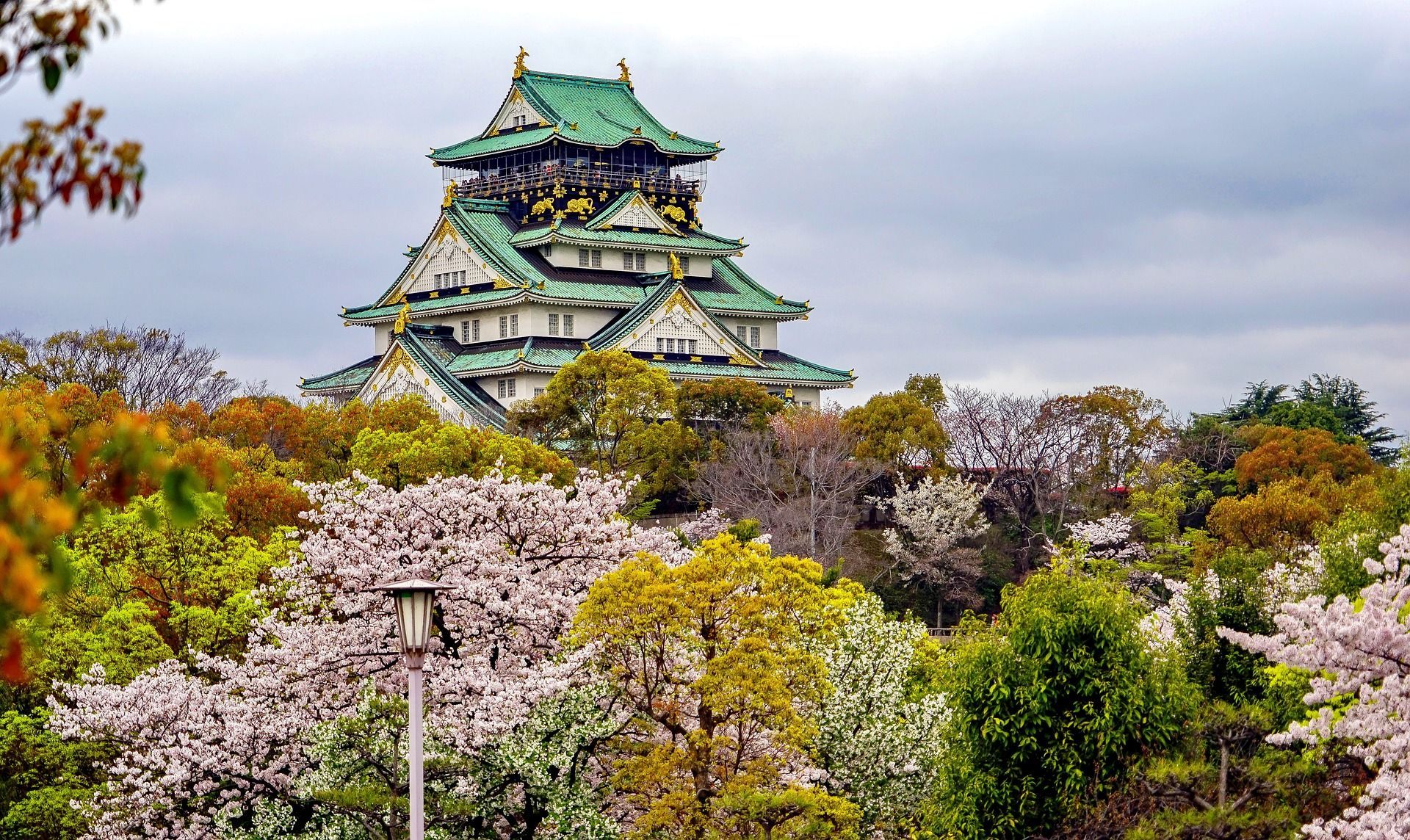 A castle is surrounded by trees and flowers on a cloudy day on Osaka, Japan