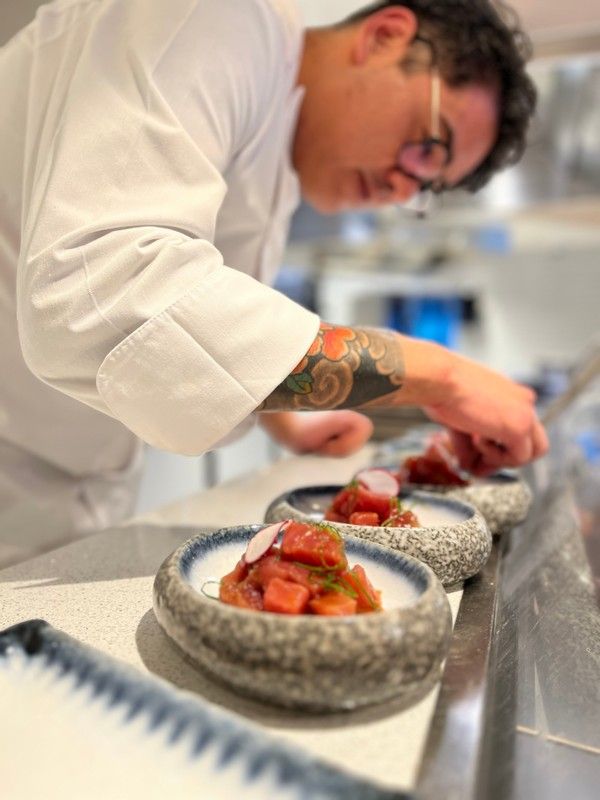 A chef with a tattoo on his arm is preparing nikkei food in a kitchen.
