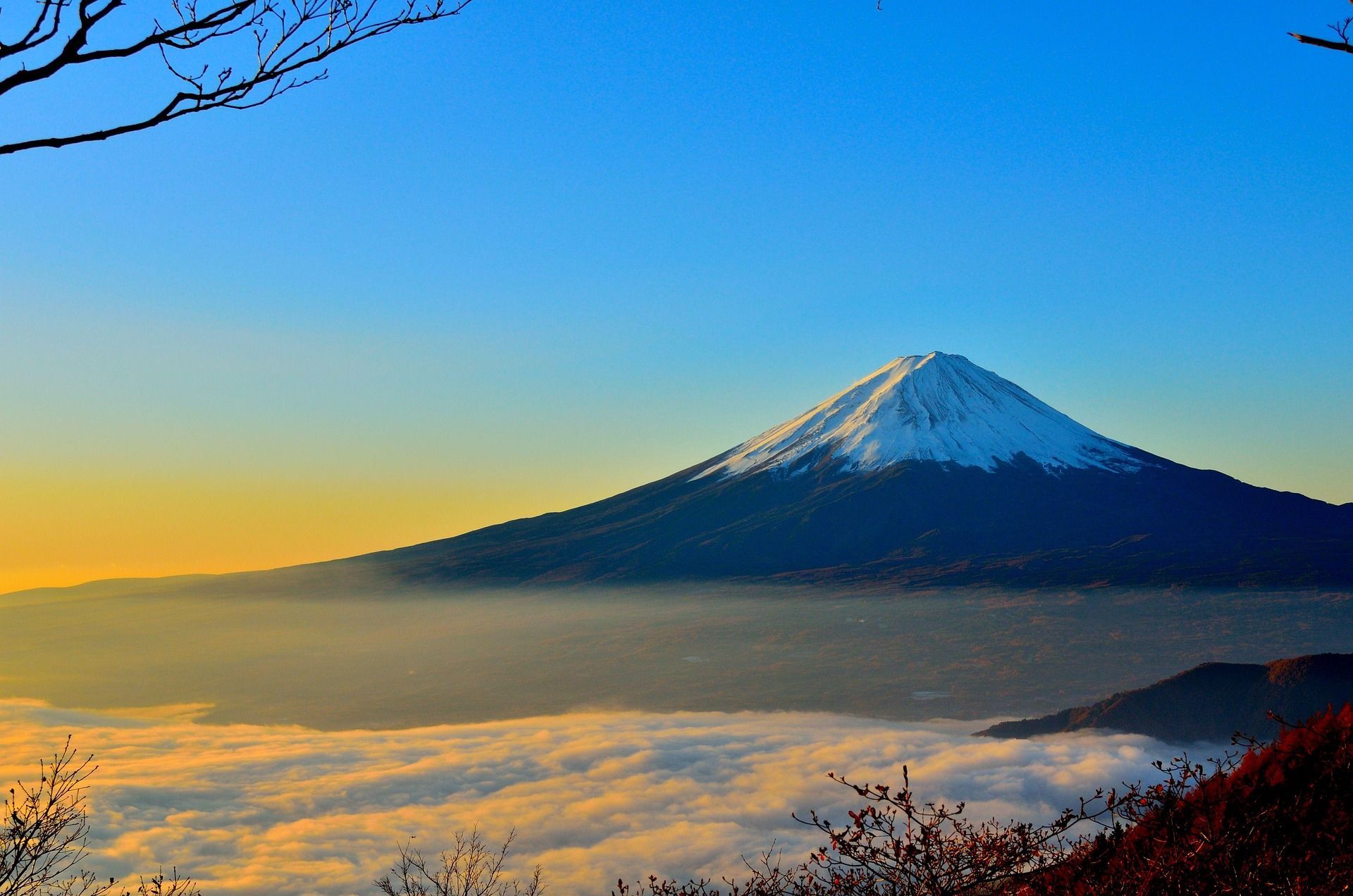 A mountain covered in snow is surrounded by clouds and trees.