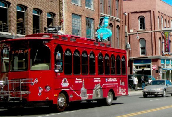 a red trolley bus is driving down a city street - Nashville Old Town Trolley Tour