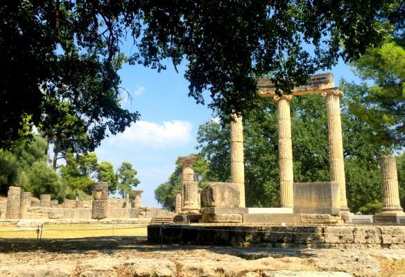 A row of columns are surrounded by trees in a park.