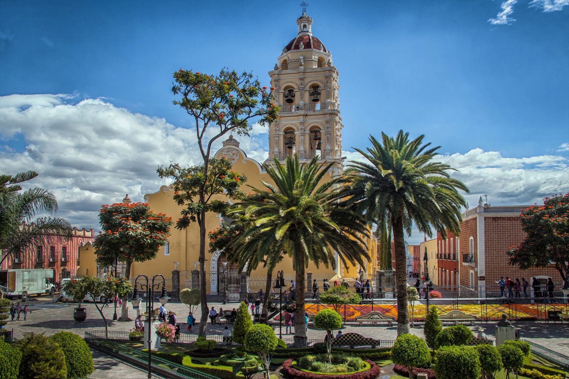 A church with a bell tower is surrounded by palm trees in a park in Puebla, Mexico