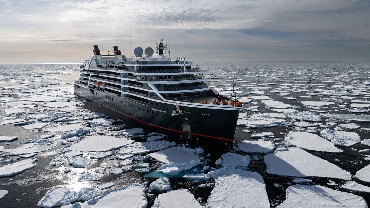 The Pole to Pole Seabourn Grand Expedition 2027 on Seabourn Venture Cruise ship navigating through sea ice under a cloudy sky. The ship is black with red accents called seabourn venture