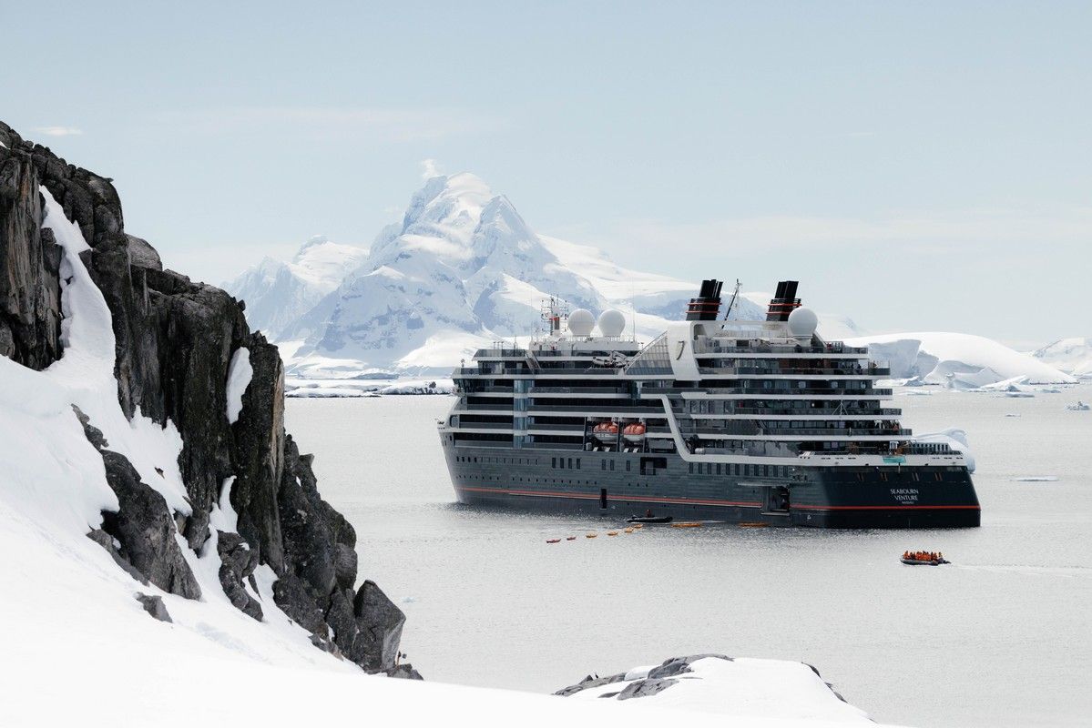 Seabourn Venture at Booth Island Cruise ship in Antarctica near snow-covered mountains and rocky cliffs. A small boat is in the water.