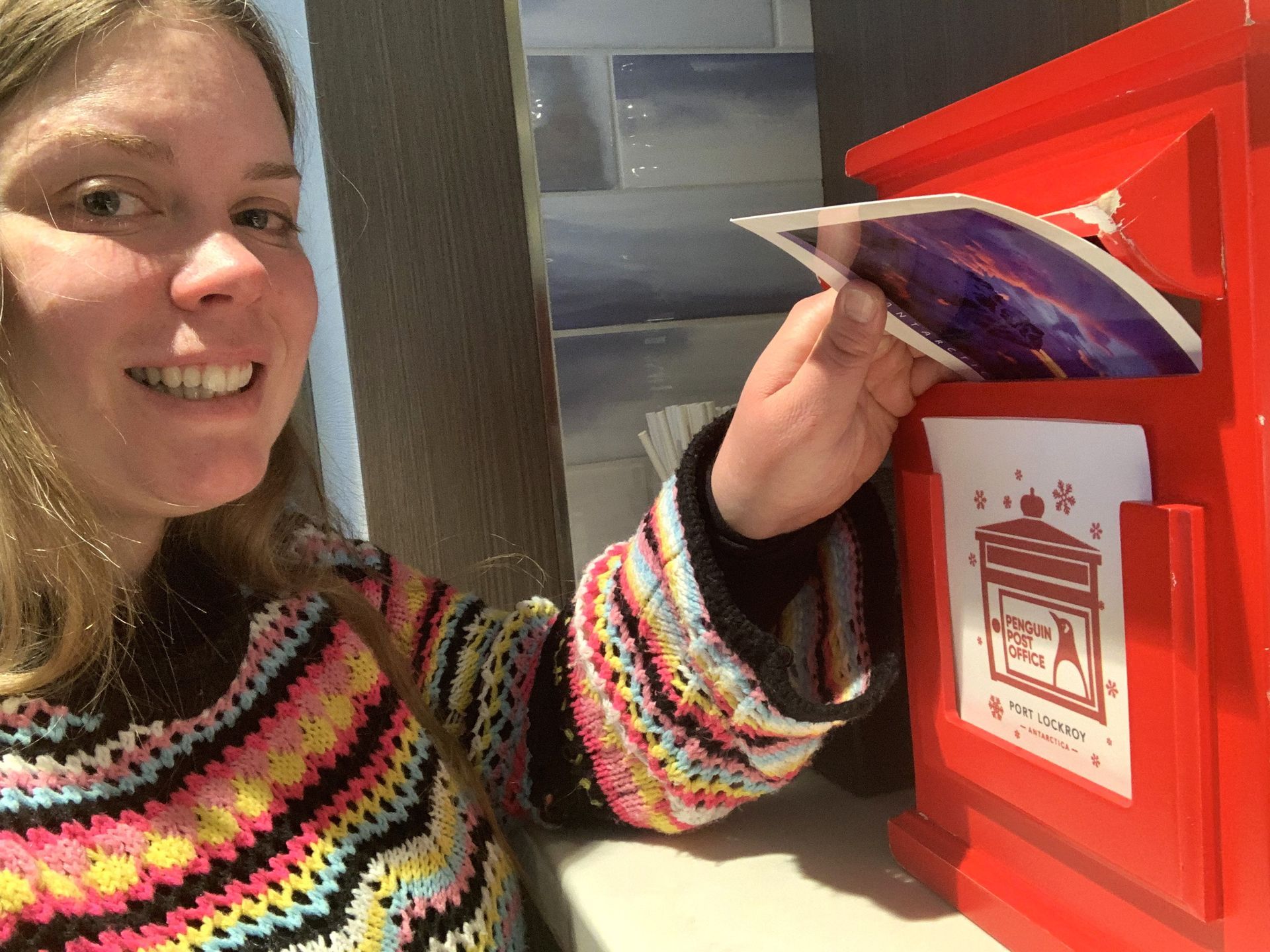 A woman is putting a card into a red mailbox.