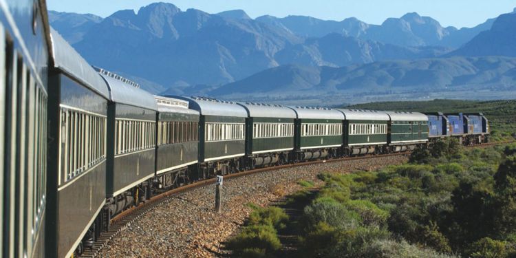 A train is going down a track with mountains in the background.