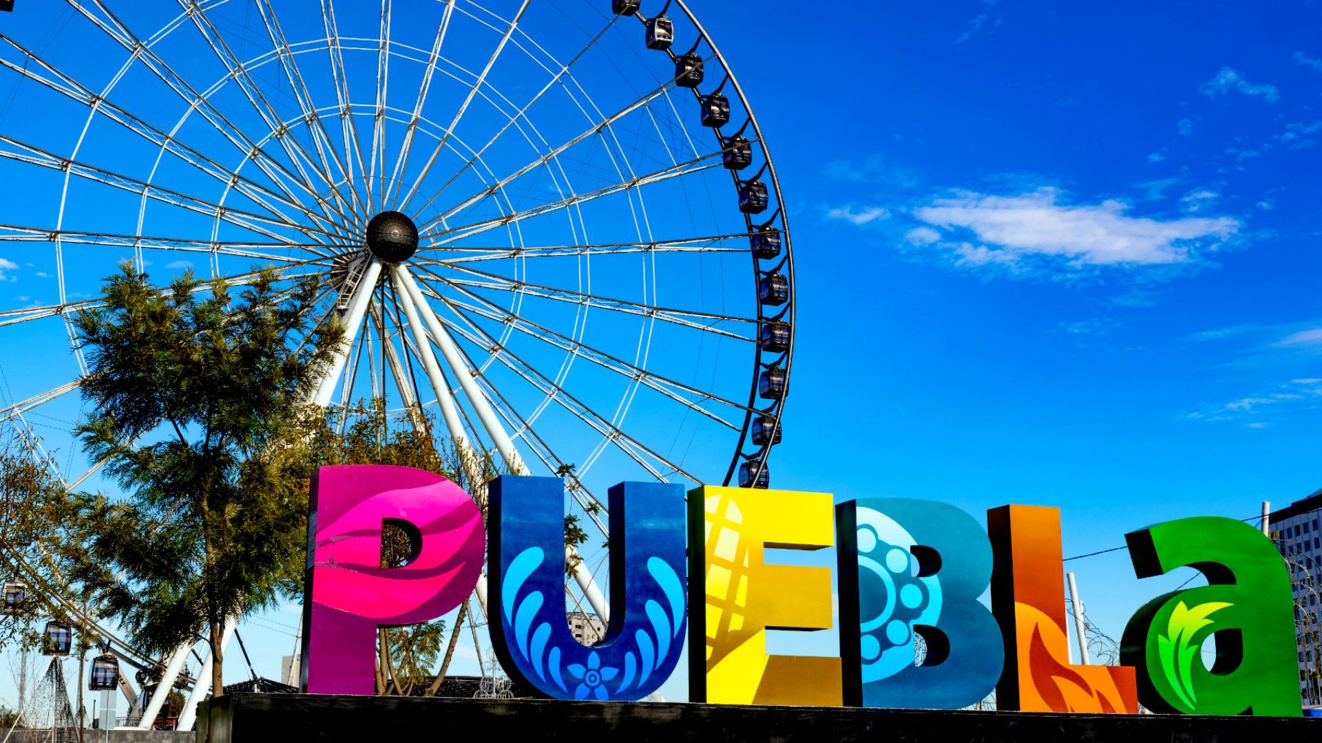a colorful sign for puebla with a ferris wheel in the background for the start of the Puebla State Fair