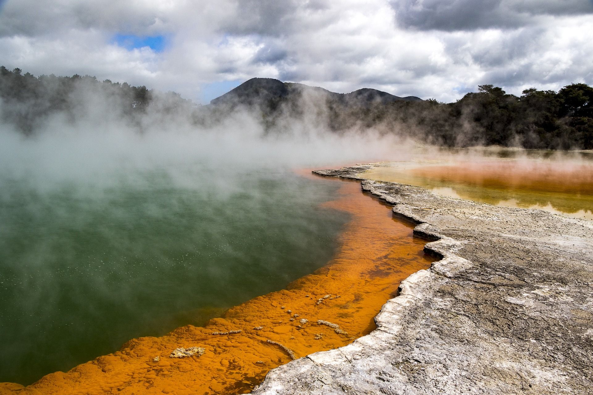 A lake with steam coming out of it and mountains in the background at Rotorua in New Zealand