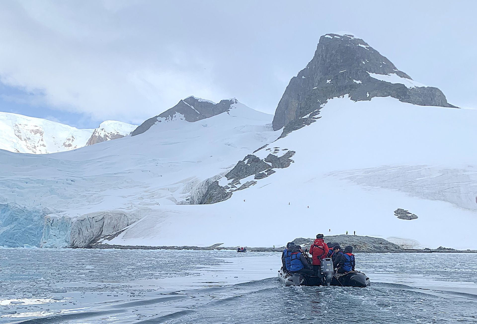 A group of people are in a boat in the water in front of a snowy mountain.