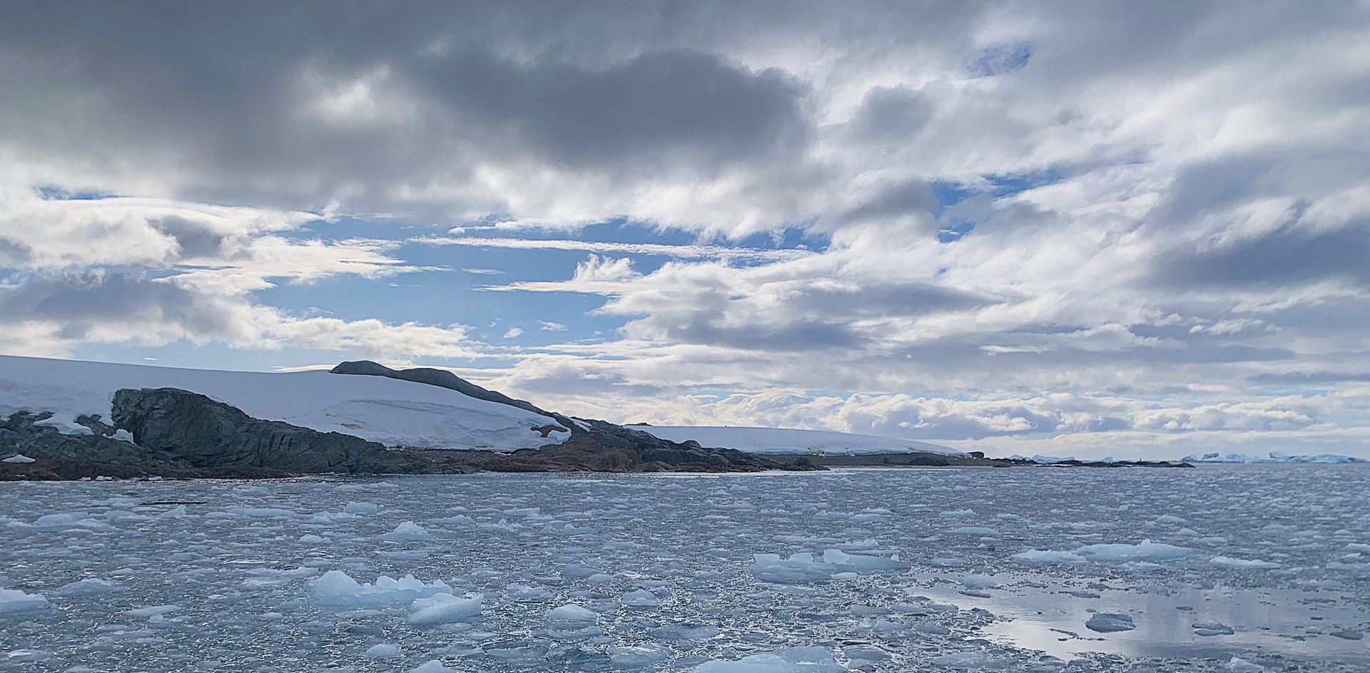 A large body of water with a mountain in the background and a cloudy sky.