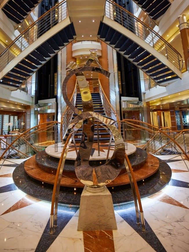 A large lobby with stairs and a sculpture in the middle on board seven seas voyager cruise ship