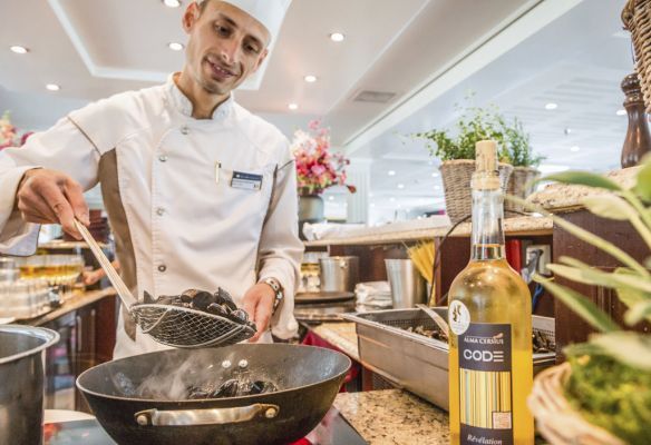 a chef is cooking food in a wok next to a bottle of wine  onboard AmaKristina