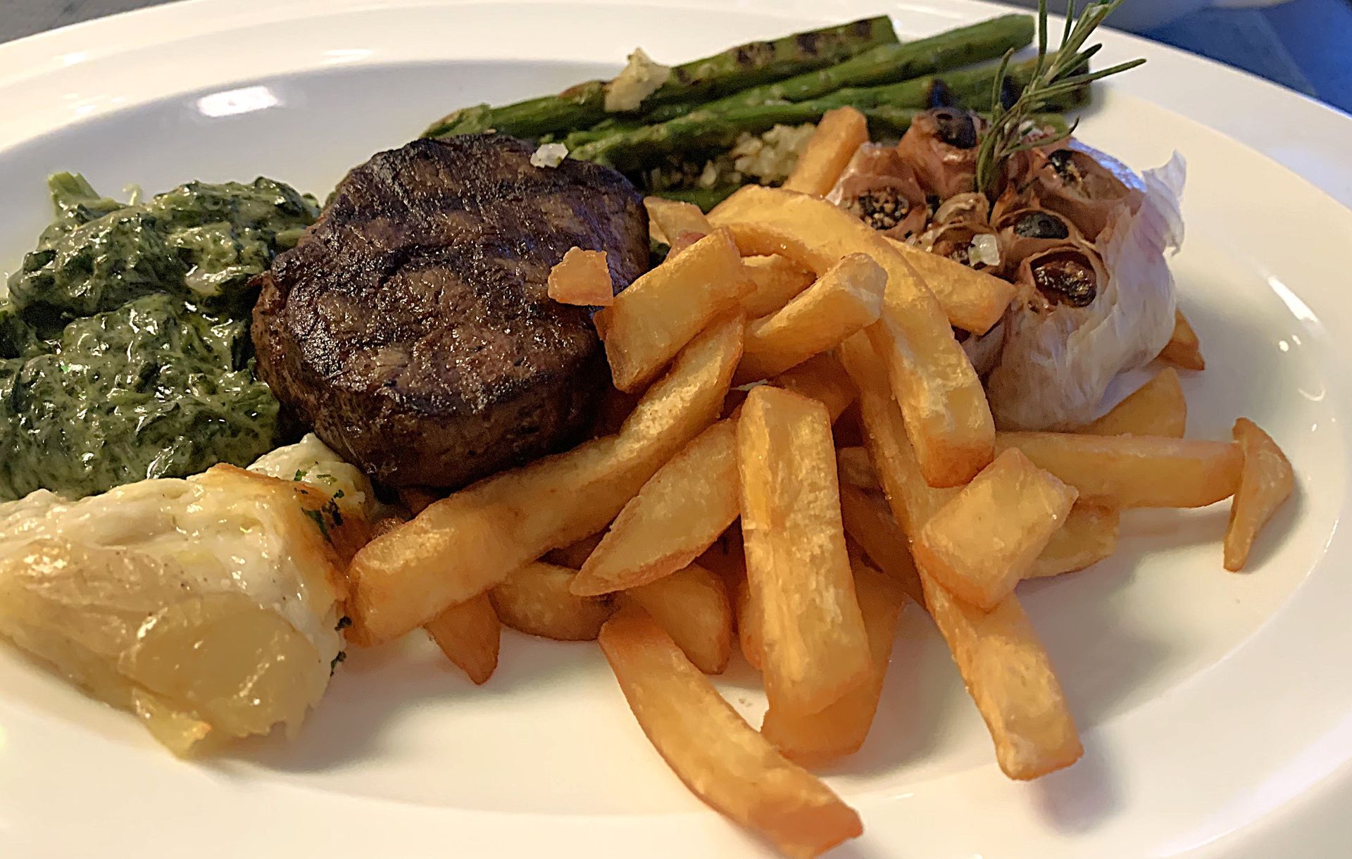 A white plate topped with a steak , french fries , spinach and garlic.