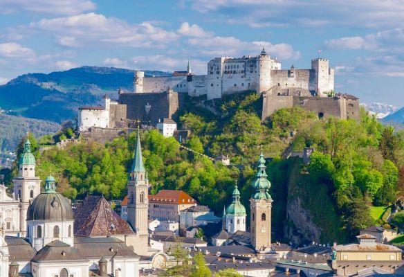 An aerial view of a city with a castle on top of a hill in the background.