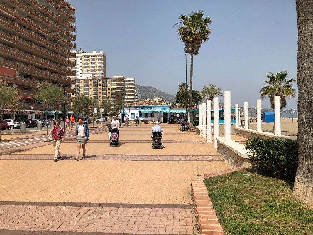 A group of people are walking down a sidewalk next to a beach with accessible access