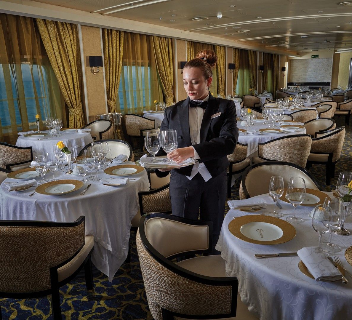 A woman in a tuxedo is serving wine glasses in a restaurant called Chartreuse