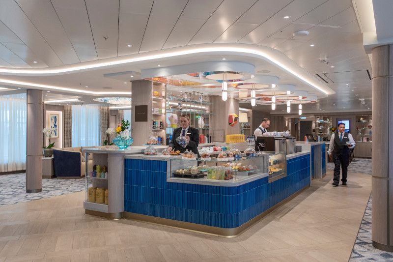 A man is standing in front of a blue counter in a restaurant called Arts Cafe on Silver Nova cruise ship
