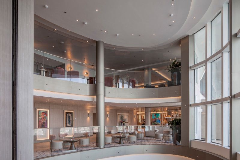 A large lobby with a lot of windows and a curved ceiling on Silver Nova cruise ship
