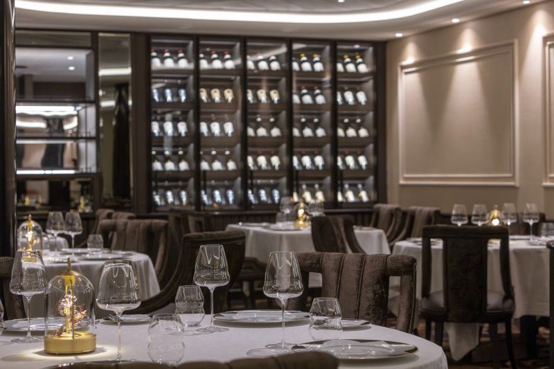 A dining room with tables and chairs and a wall of wine bottles at La Dame on Silver Nova cruise ship