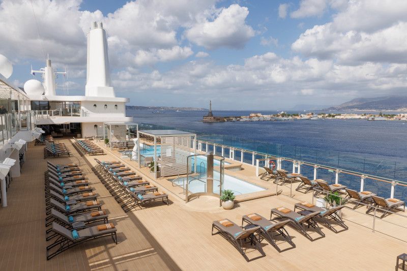 A large cruise ship with a swimming pool and lounge chairs on the deck on Silver Nova cruise ship