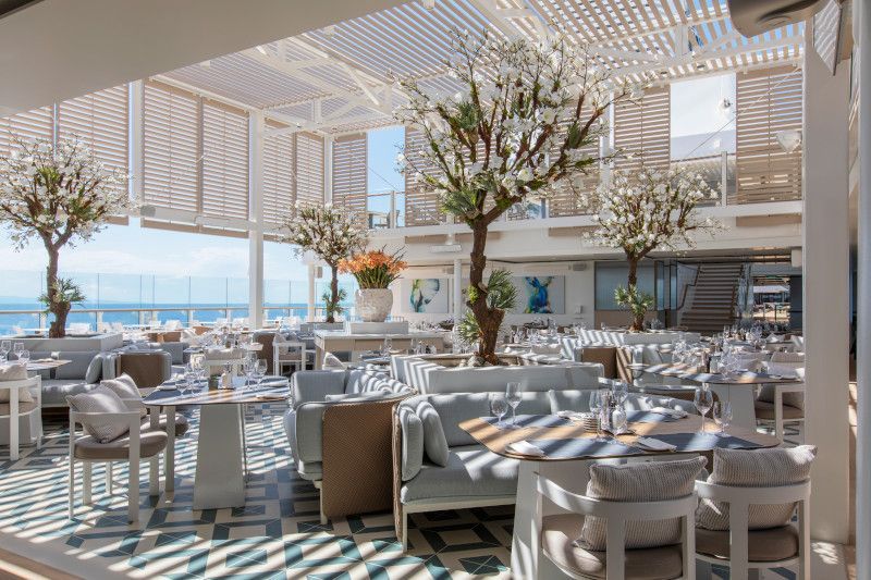 A restaurant with tables and chairs and a view of the ocean.