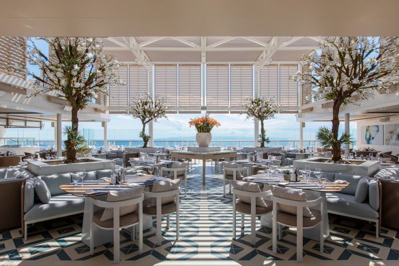 A large dining room with tables and chairs and a view of the ocean.