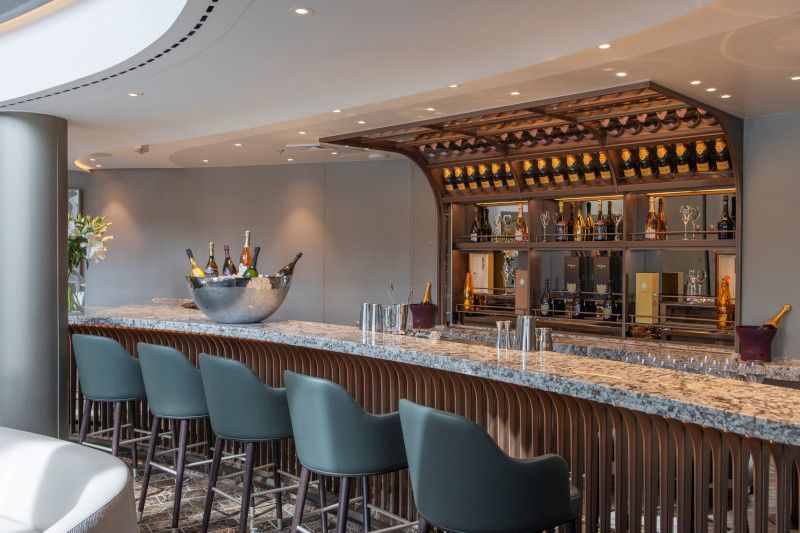 A long bar with chairs and bottles of wine on it.
