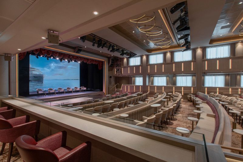 A large auditorium with rows of seats and a stage on a cruise ship.