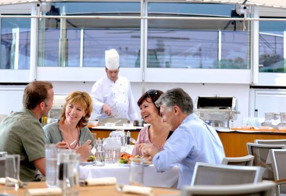 a group of people are sitting at a table with a chef in the background at the Sky Grill on Avalon Envision