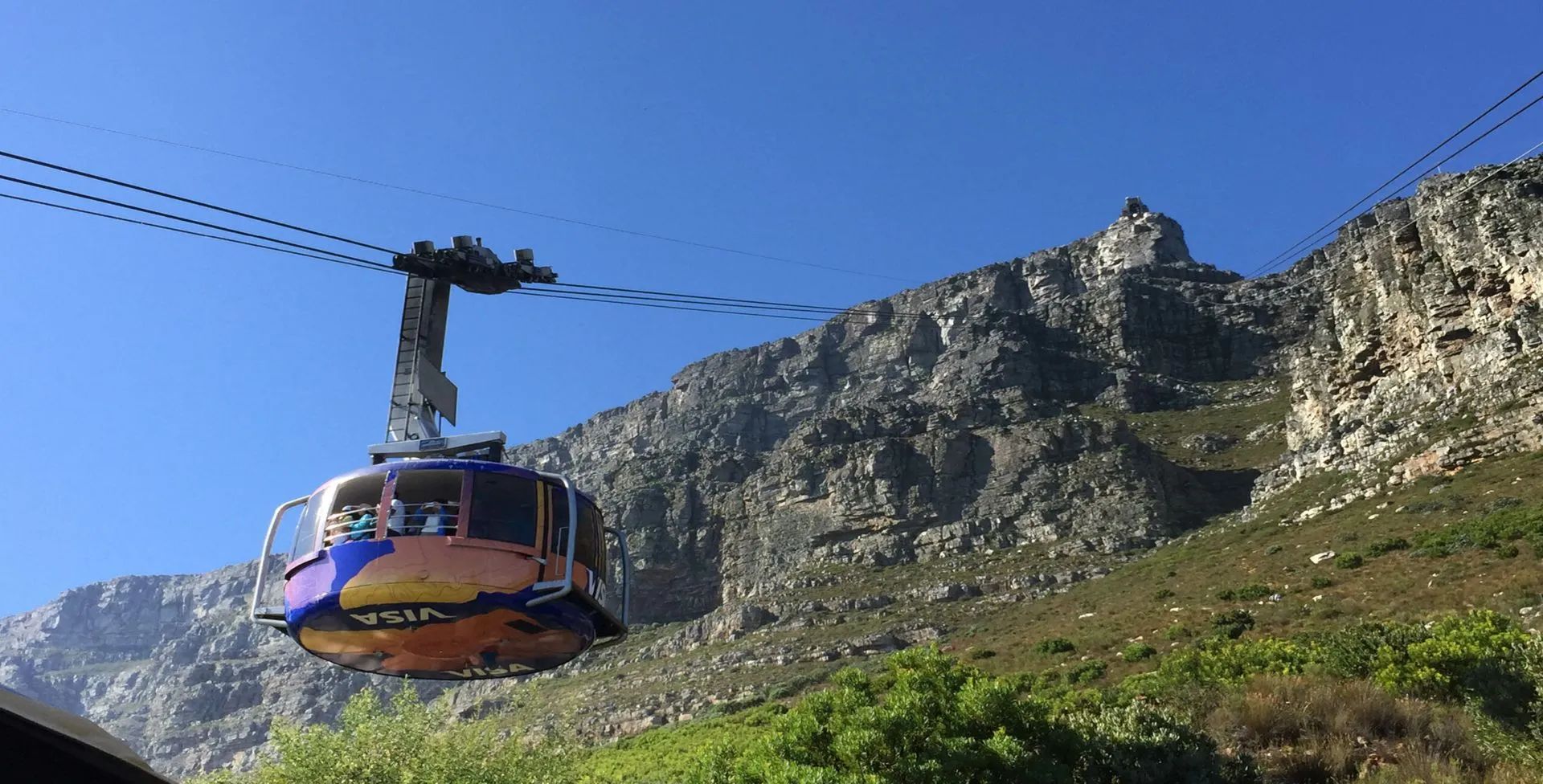 Cable car ascending Table Mountain, Cape Town, with a rugged mountain backdrop and blue sky.