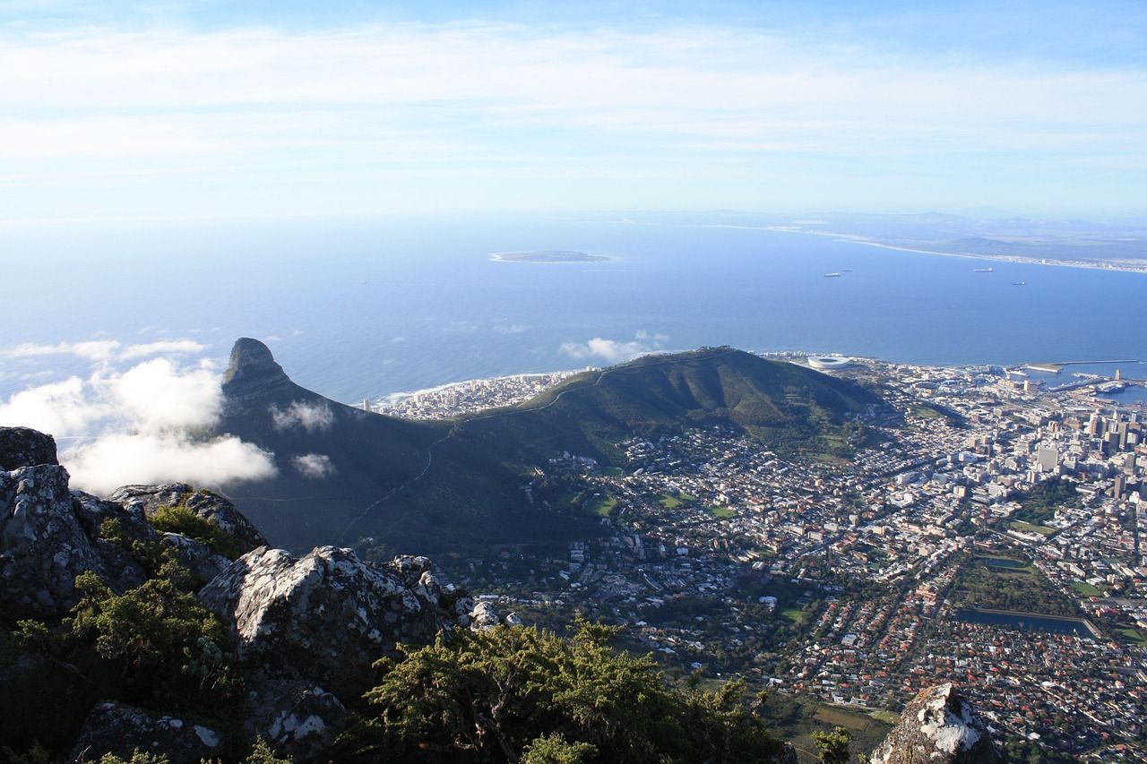 View from a mountain summit overlooking Cape Town, South Africa, with Lion's Head prominent and the ocean in the distance.
