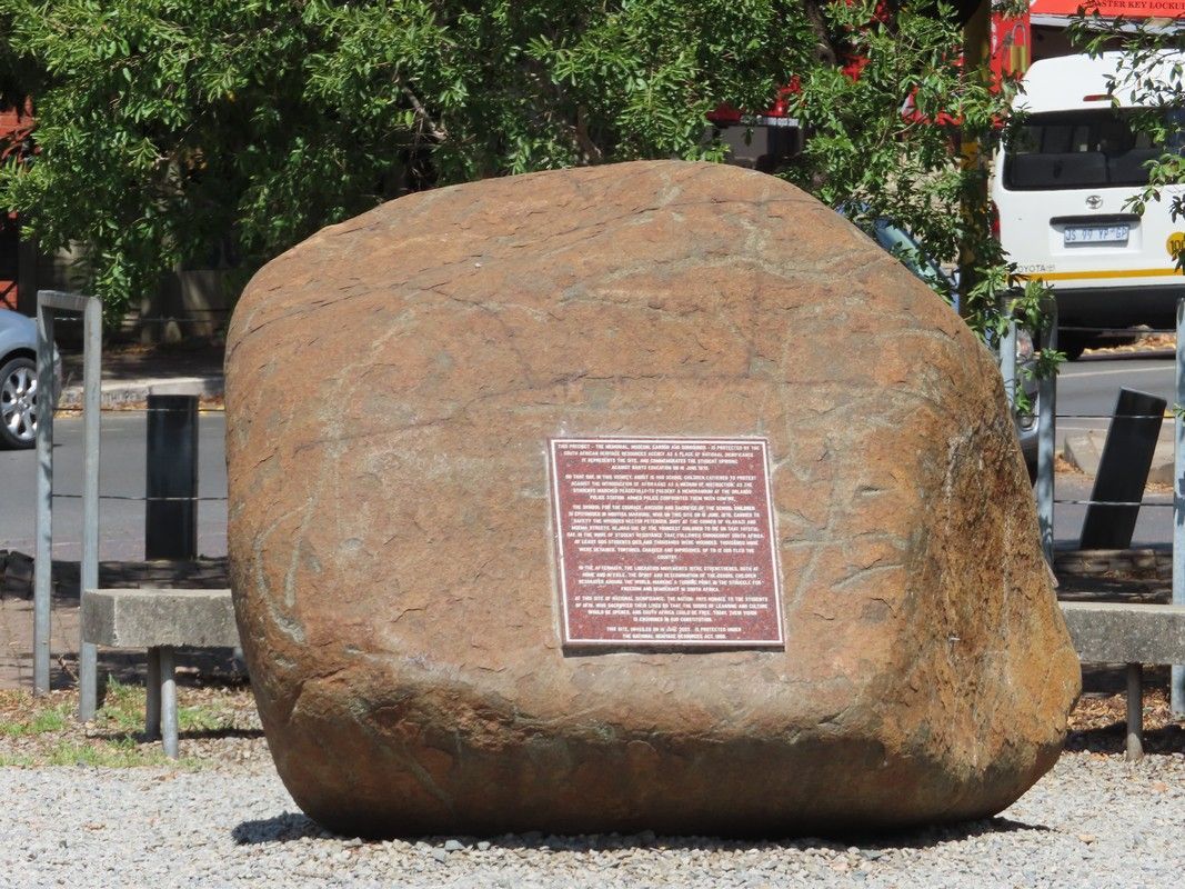 A large rock with a plaque on it is sitting on the side of the road.