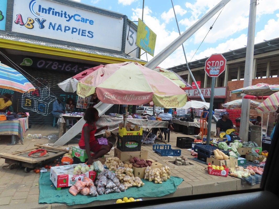 A woman is sitting under an umbrella at a market.