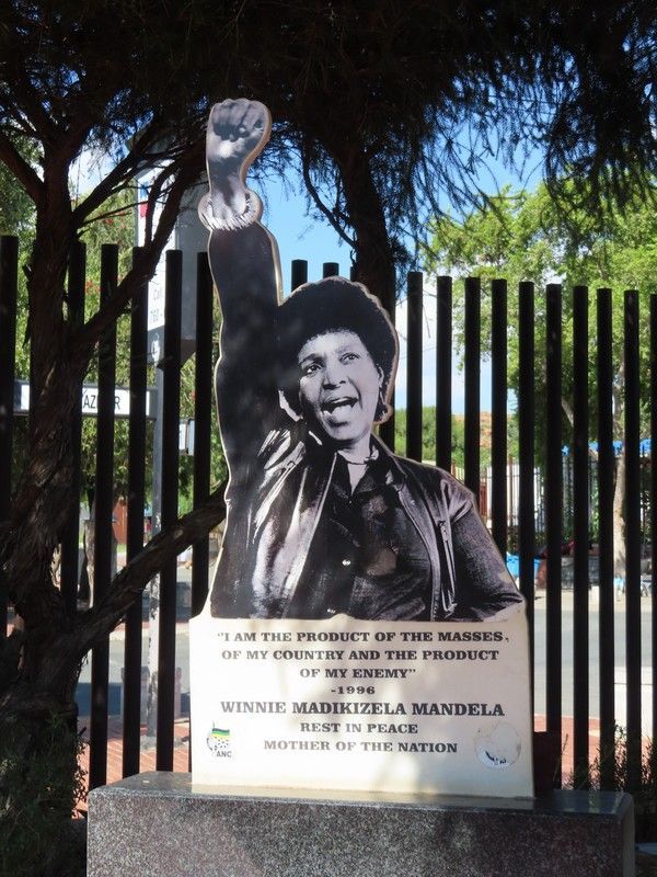 A statue of minnie mandela is standing in front of a fence
