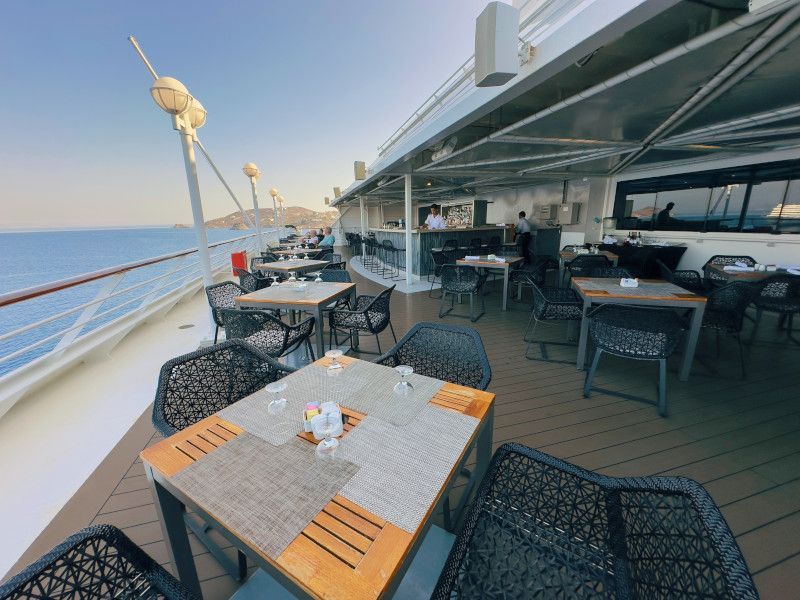 There are many tables and chairs on the deck of a cruise ship at the sunset bar