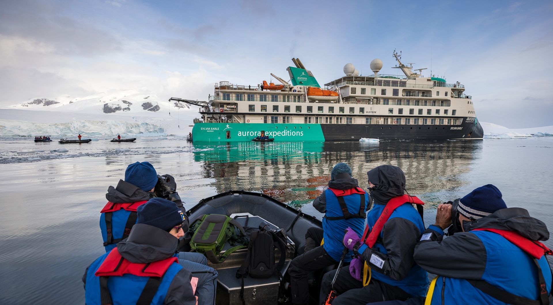 A group of people are sitting in a boat in front of an expedition cruise ship.