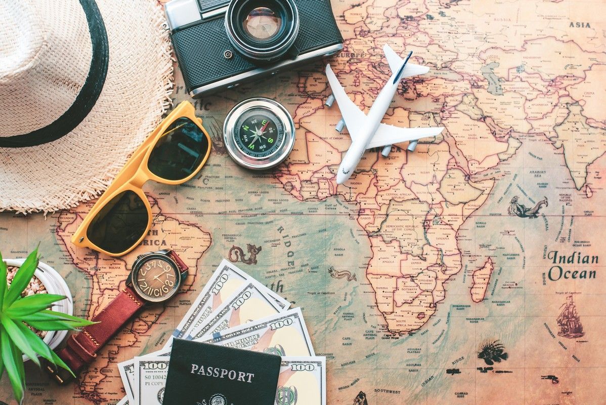 A map with a hat , sunglasses , money , a camera , and a plane on it.