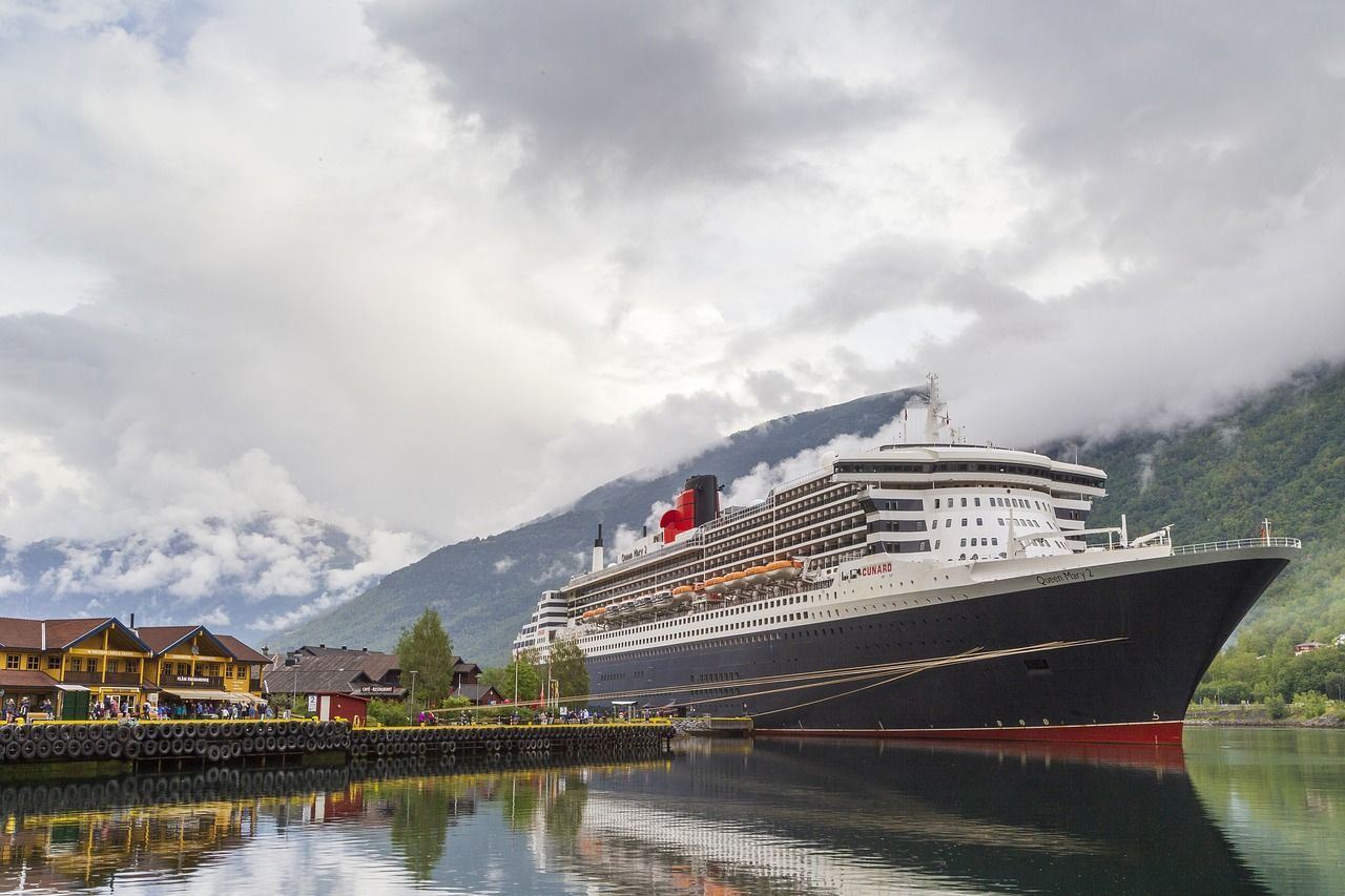 A large cruise ship is docked in a harbor with mountains in the background.