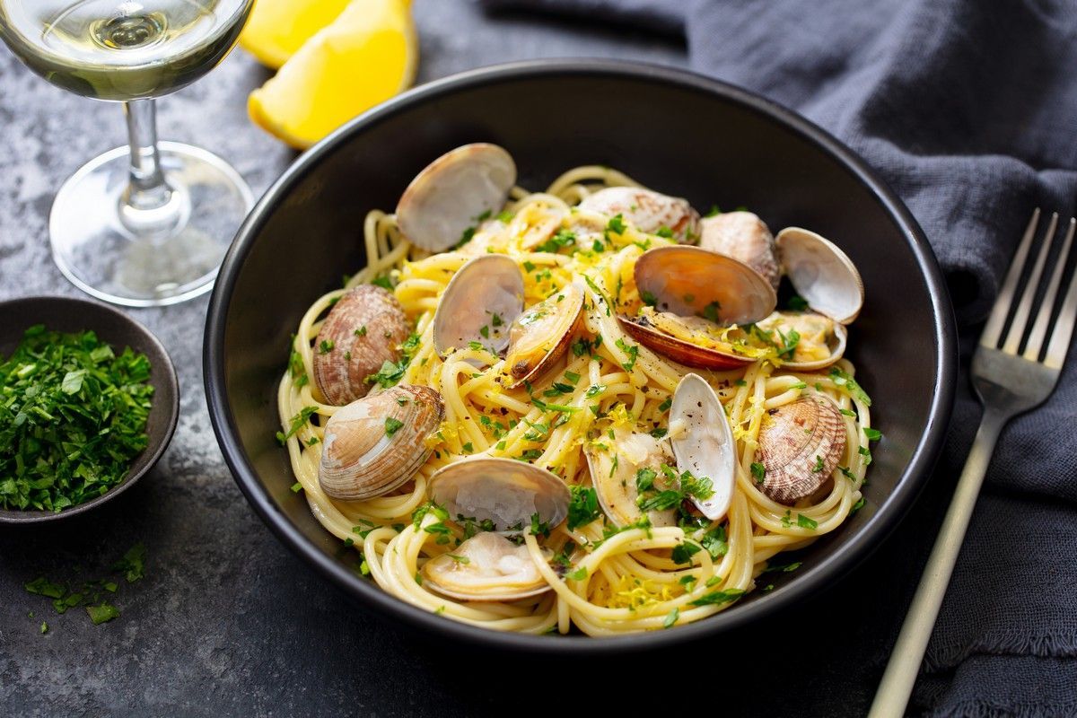 A bowl of spaghetti with clams and a glass of wine.