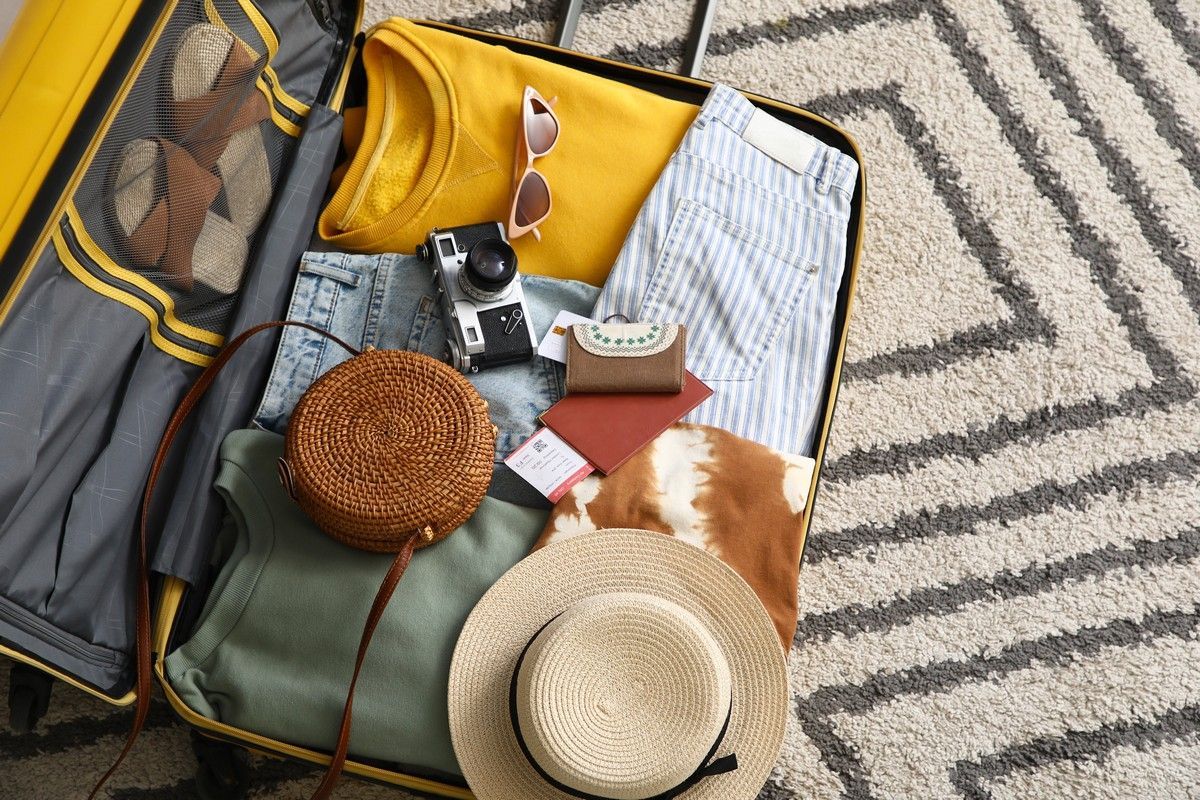 A suitcase filled with clothes and a hat is sitting on a rug.