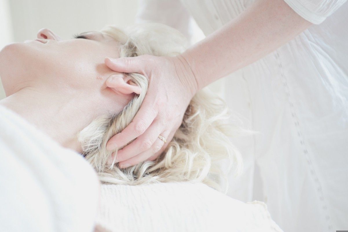 A woman is getting a head massage from a woman in a white dress.