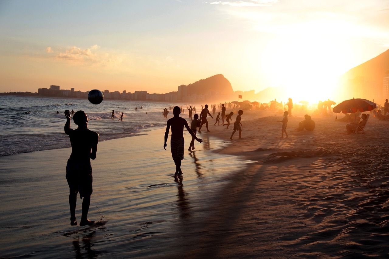 A group of people are playing soccer on copacabana beach at sunset.