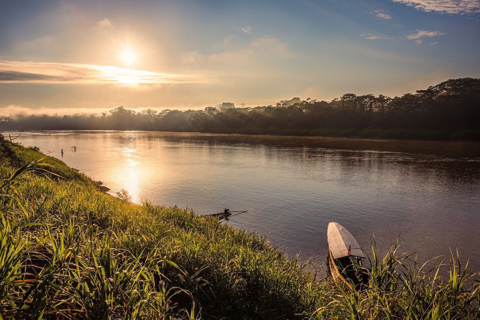 A boat is sitting on the shore of a river at sunset at Tambopata National Reserve