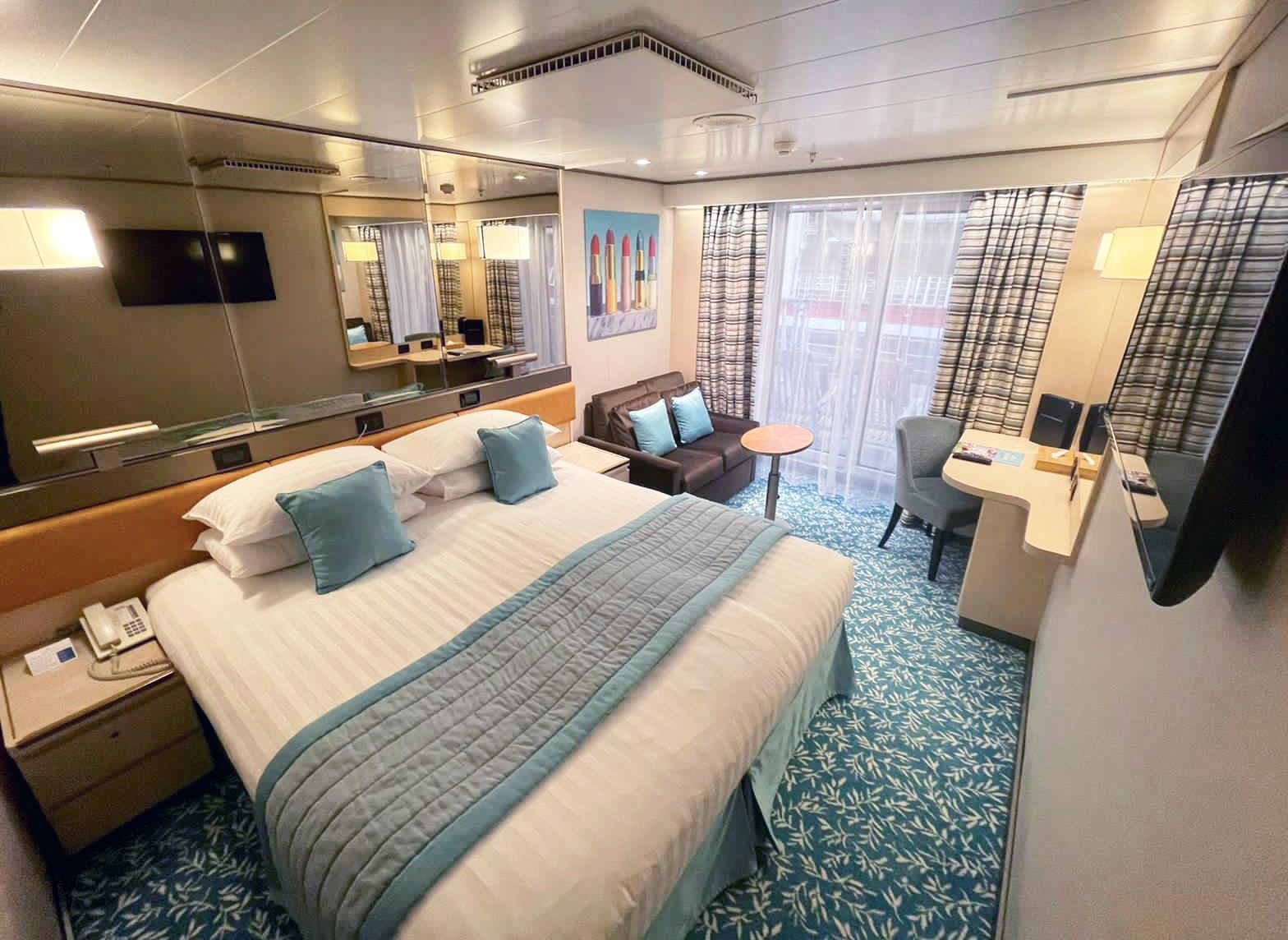 A cruise cabin room with a bed , couch , desk and television.