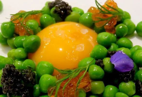 A close up of a plate of food with peas and an egg