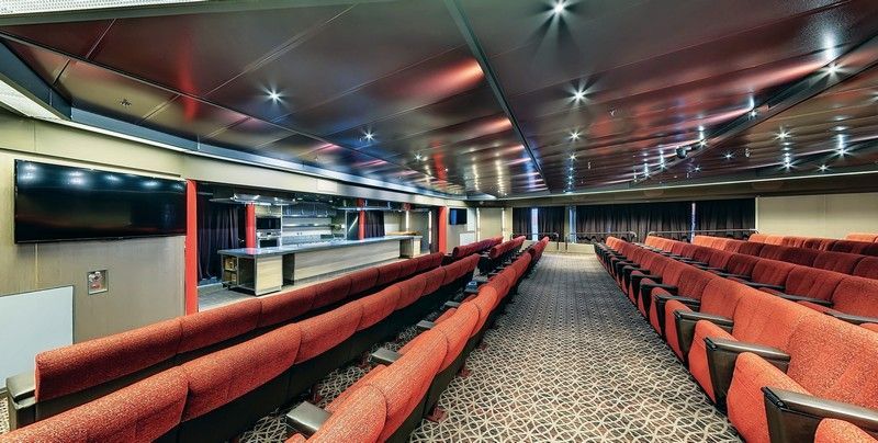 There are a lot of red chairs in this Auditorium room.