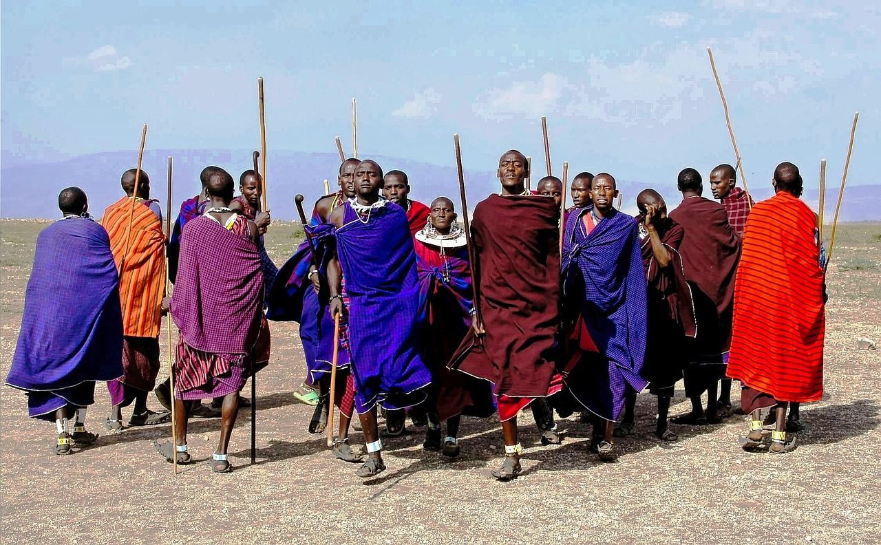 Maasai Mara, Kenya A group of Maasai warriors in colorful robes and spears in a field, with mountains in the background.