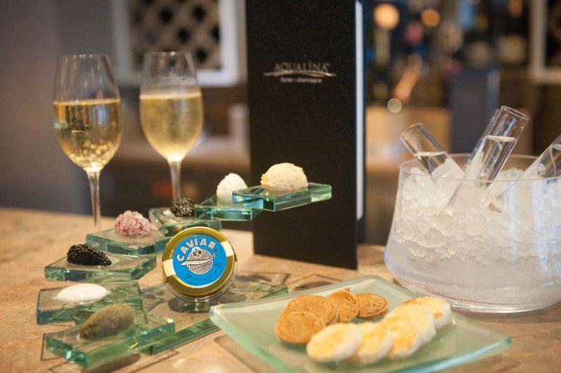 A table topped with plates of food and glasses of wine and a tin of caviar