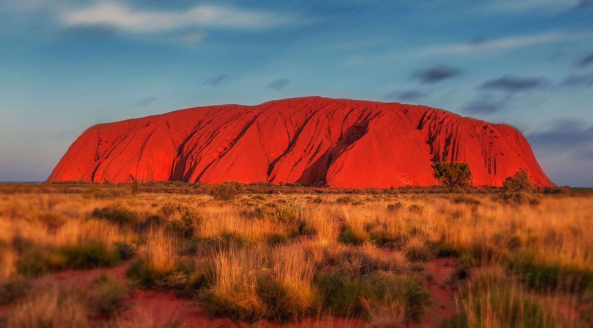 A large red rock formation in the middle of a desert in Australia known as Uluru 