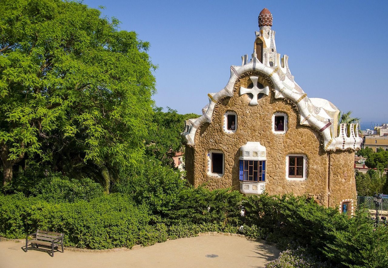 A stone building with a cross on the roof is surrounded by trees and bushes